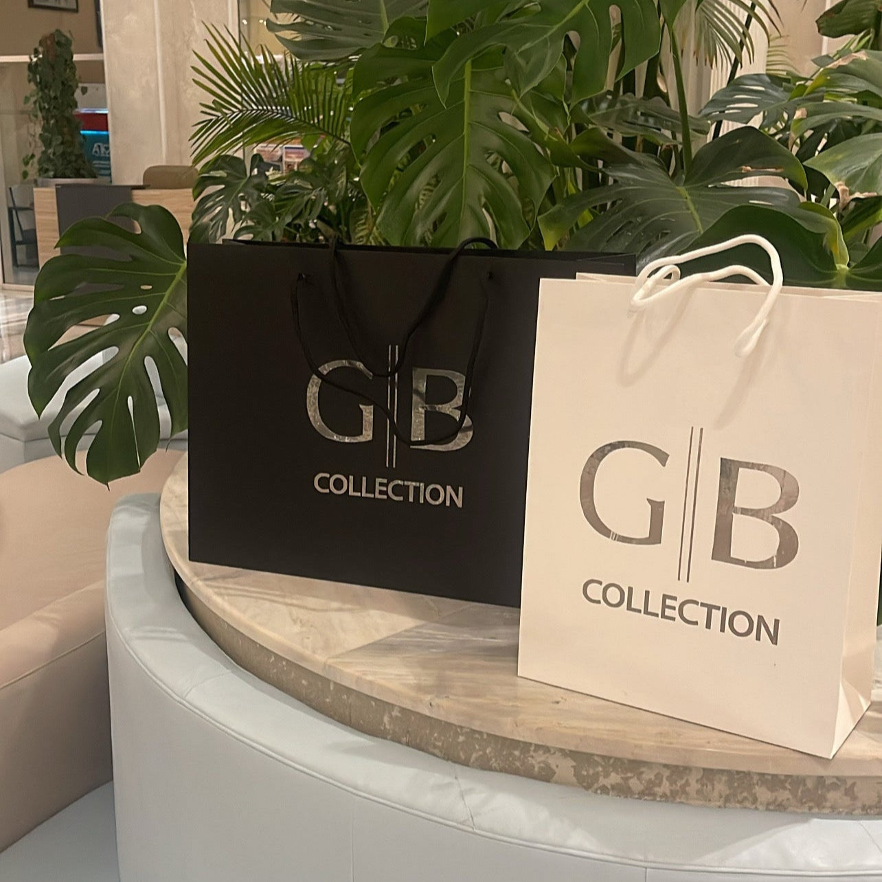 Two GB Collection bags on a round white table with plants in the background.