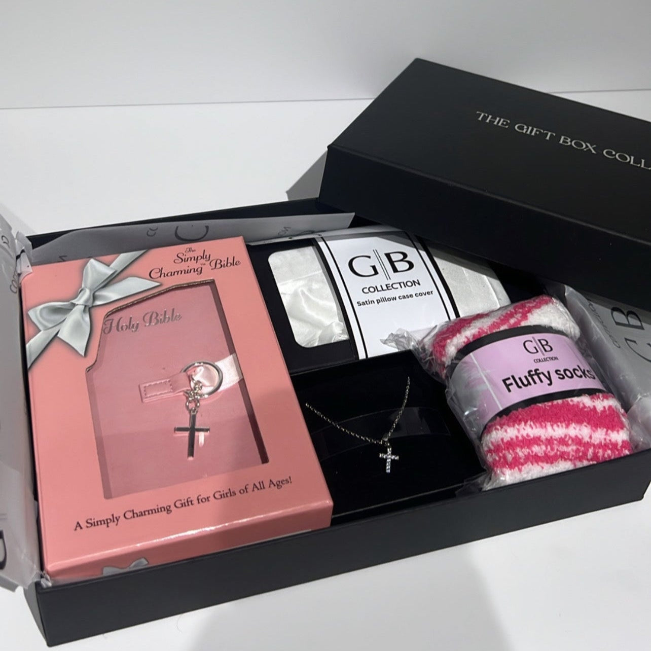 Gift set with pink book, necklace, and socks in a black box on a white background