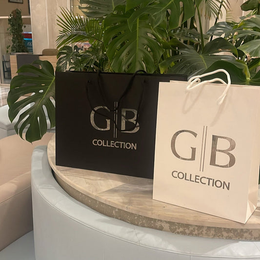 Two GB Collection bags on a round white table with plants in the background.